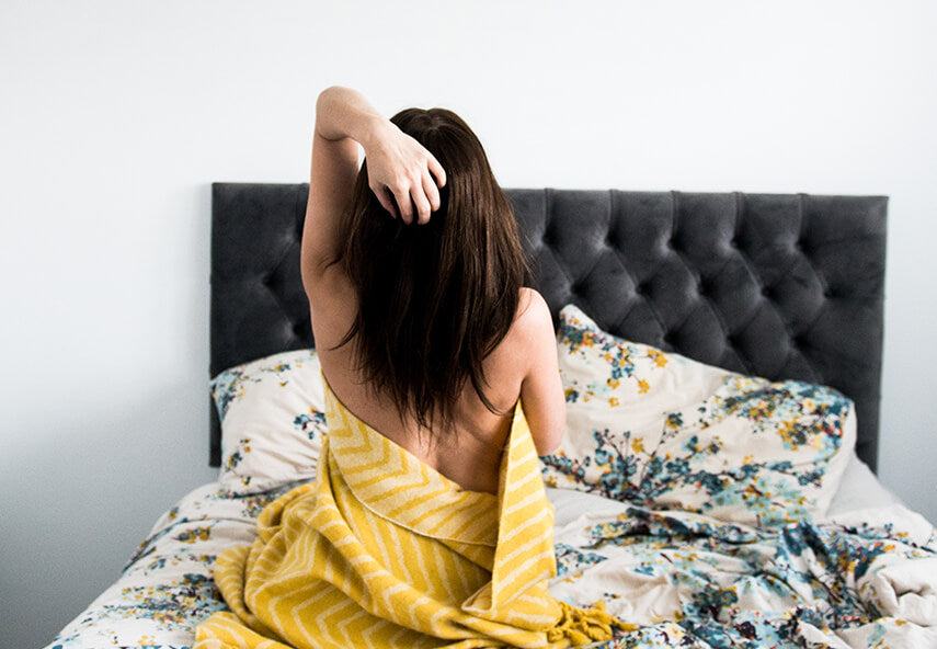 Woman sat on a bed with her back to the camera holding her hair